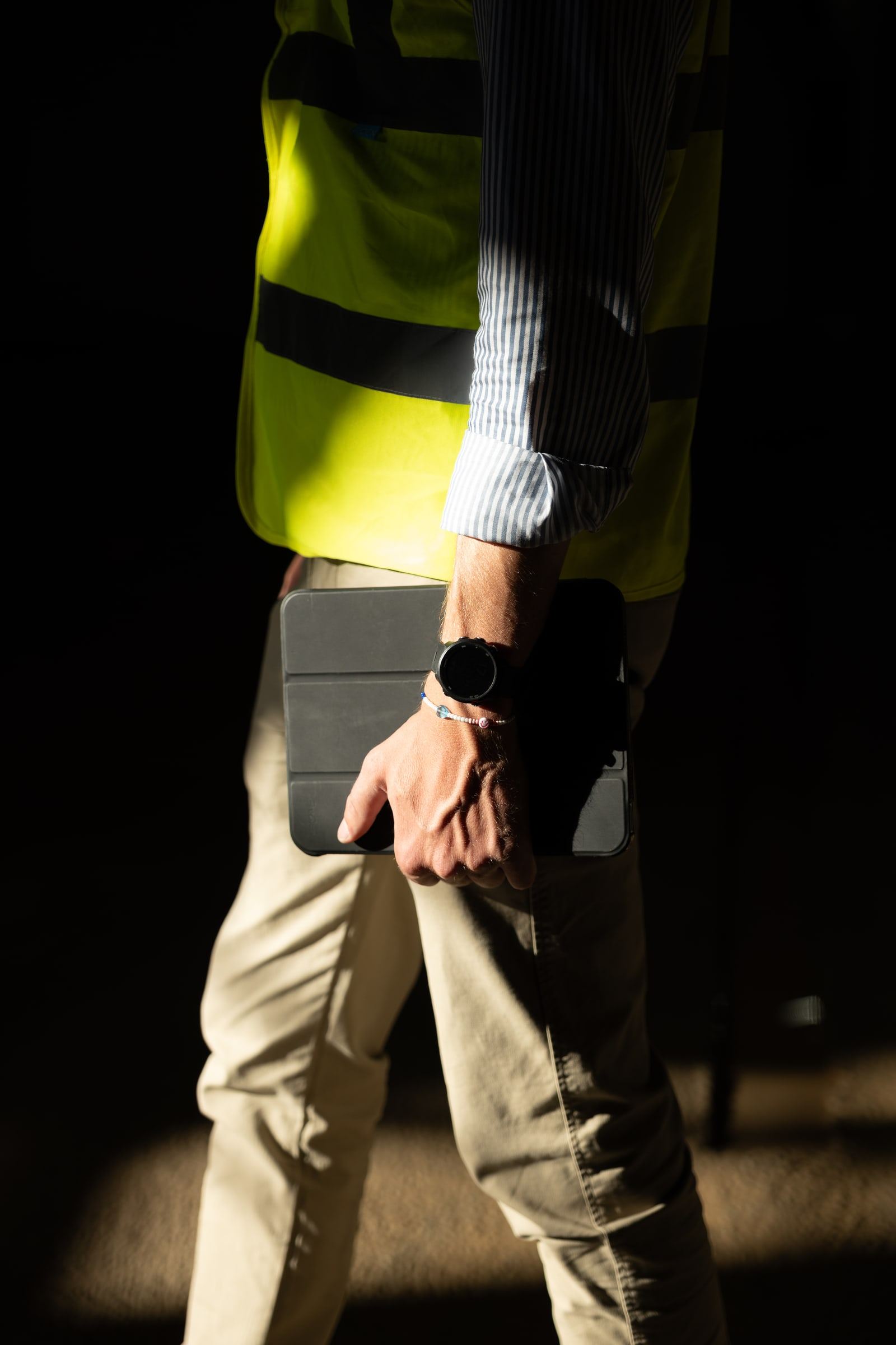 Engineer in a hi-vis vest holding a tablet in raking light on site